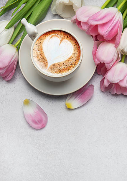 istock Cappuccino with heart shaped foam and pink tulips bouquet on grey table 2207127437