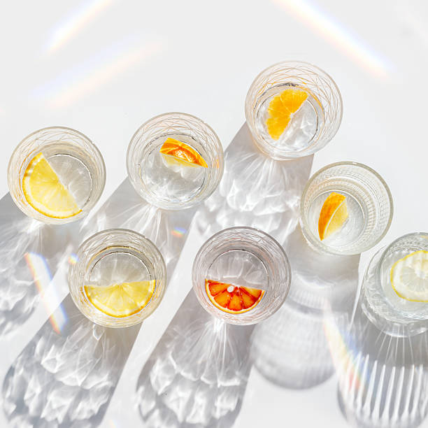 istock Fruit Infused Water in transparent Glasses with Shadows at sunlight on White background. Aesthetic view summer healthy drink with slices of lemon, orange with rainbow sun glare from glass cups, above 2207129105