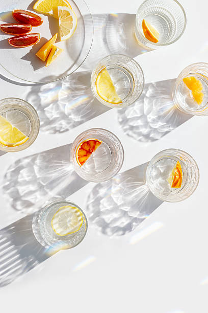istock Crystal glasses with citrus slices in water on white background with rainbow reflections at sunlight, modern, minimal composition with glass cups filled with water and citrus fruit, as lemon orange 2207129113