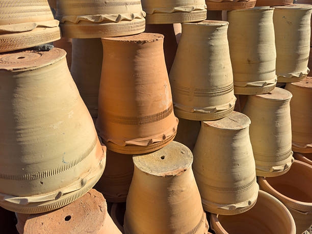 This image features a hand with brown skin holding up a small, traditional clay pot against a clean white background. The earthen pot, also known as a matka or ghada, is a classic example of handmade pottery often used in South Asian cultures for storing and naturally cooling water. The isolated shot emphasizes the rustic texture of the pot and the simple, functional design.