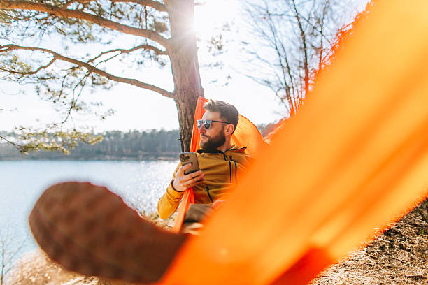 istock Handsome Man with Smartphone in Lakeside Hammock During Spring 2207132089