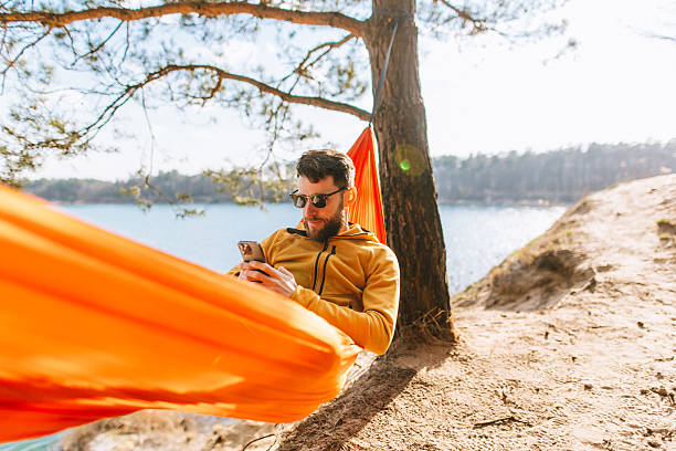 istock Handsome Man Texting on Social Media in Lakeside Hammock on Sunny Spring Day 2207132128