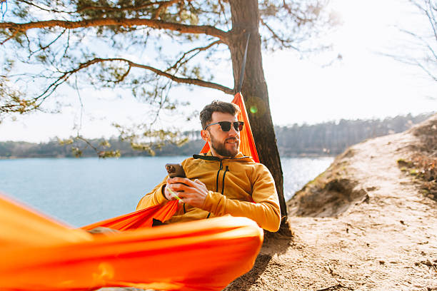 istock Digital Detox Delight: Cheerful Man Relaxes in Hammock with Smartphone on Sunny Spring Day 2207132154