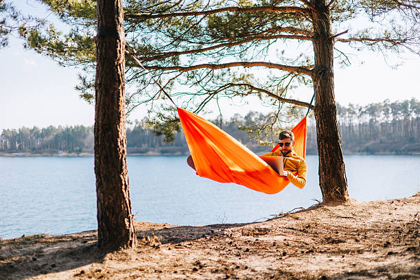 istock The Ultimate Remote Office: Man Works from Hammock by a Sunlit Spring Lake 2207132346