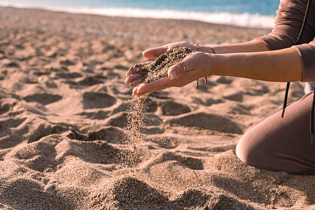 istock Hands releasing beach sand during sunset on a tranquil shoreline 2207133375