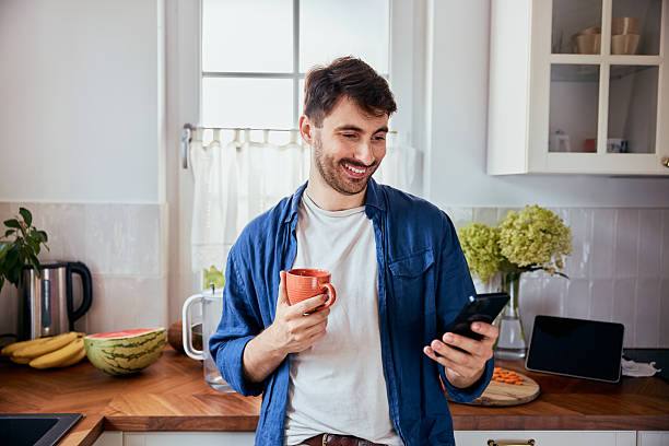 istock Portrait of young man in kitchen using mobile phone while having coffee 2207138232