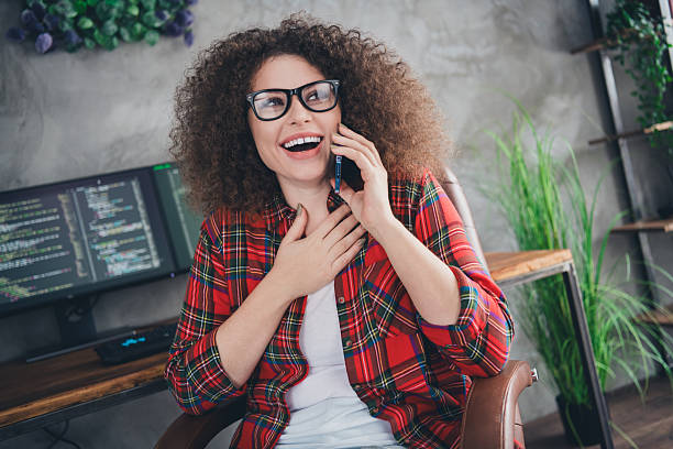 istock Young woman programmer with curly hair smiling while enjoying a phone conversation in a casual workspace with coding on the screen. 2207139624