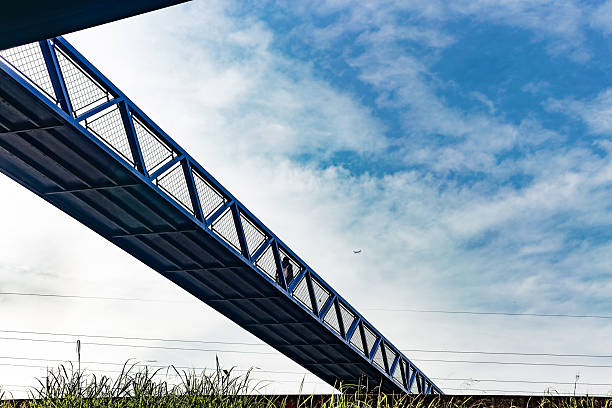 Madrid. Spain. Capturing a low angle view of a modern blue steel pedestrian bridge rising against a backdrop of dramatic clouds in the sky