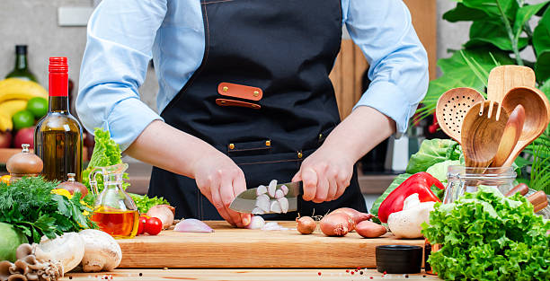 istock Chef cuts shallots onion in cozy kitchen with wooden table, kitchenware, vegetables, herbs and ingredients for cooking. Healthy vegan food, culinary, recipes, blogging 2207149769