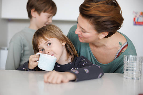 istock Caring mother caressing daughter at the kitchen counter, her son hanging around 2207152049