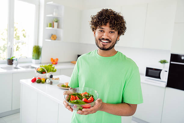 istock Young man in a modern kitchen holding a fresh salad, smiling happily, daylit interior 2207152929