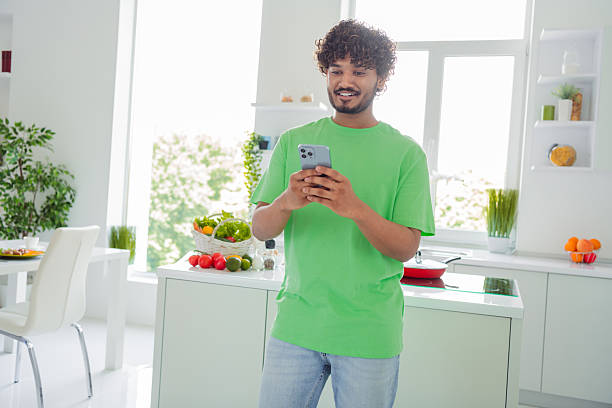 istock Young Multiethnic Man Reading Phone in Bright Kitchen While Preparing a Meal 2207153006