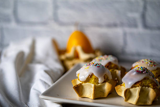 A plate of pastries with icing and sprinkles on top. The plate is on a white cloth. The pastries are named pardulas and are typical easter sweets of sardinia