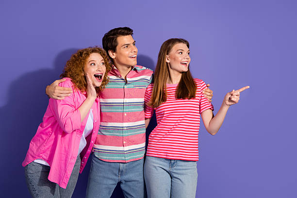 istock Three young friends laughing together while pointing and gesturing on a vibrant purple background, showcasing friendship 2207154031