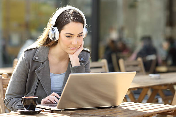 istock Woman using laptop and headphone in a bar terrace 2207154208