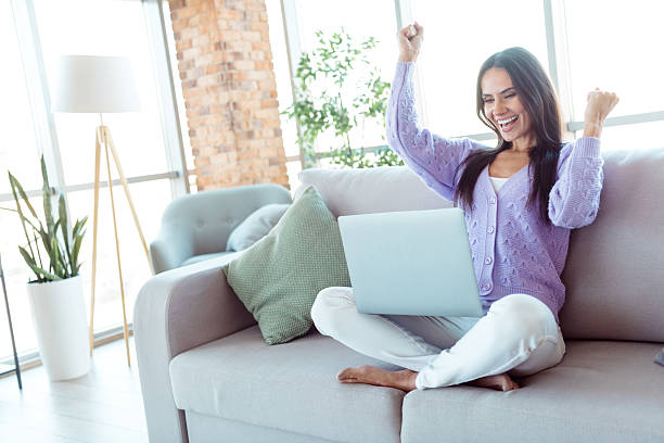 istock Young woman celebrating success while using laptop at home in a stylish loft setting with bright daylight highlighting modern interior 2207154857