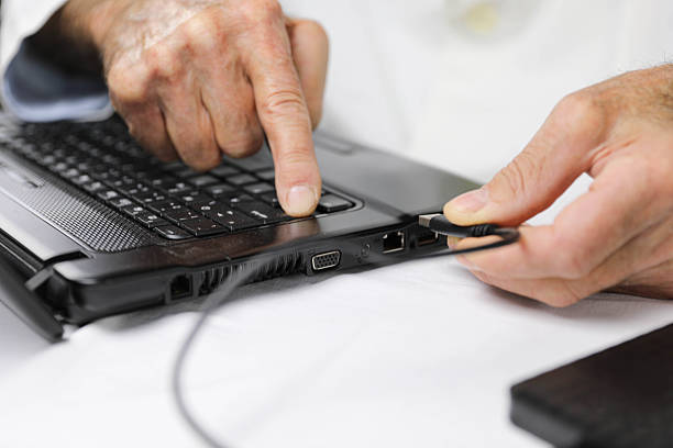istock Senior Male Doctor Plugging USB Flash Drive into Laptop – Close-Up 2207157017