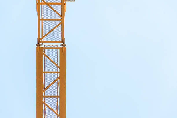 Close-up view of an orange construction crane's metal truss structure against a clear, pale blue sky. The shot emphasizes the geometric shapes and industrial design of the crane. Ideal for illustrating concepts of construction, engineering, infrastructure, or industrial strength.