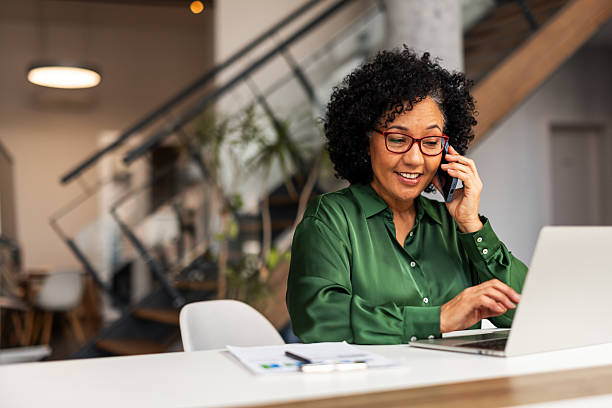 istock Professional Woman Smiling While Using a Laptop and Smartphone at Office Desk 2207162099