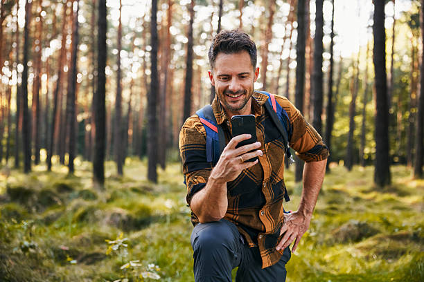 istock Smiling adult man using mobile phone while hiking in forest 2207163753