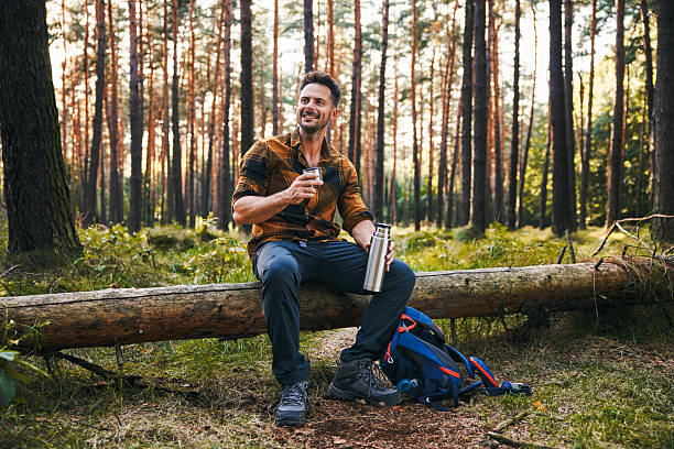 istock Male hiker resting in forest sitting on tree drinking 2207163784