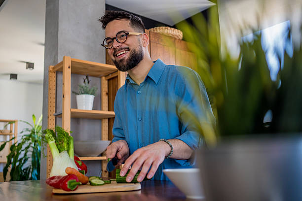 istock A young, smiling man in the kitchen is cutting vegetables on a board, radiating joy and relaxation. 2207165218
