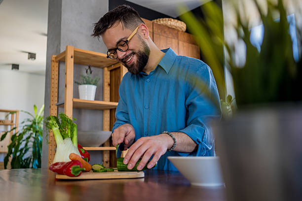istock A young, smiling man in the kitchen is cutting vegetables on a board, radiating joy and relaxation. 2207165219