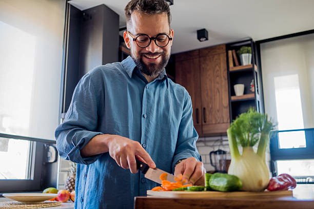istock A young, smiling man in the kitchen is cutting vegetables on a board, radiating joy and relaxation. 2207166927