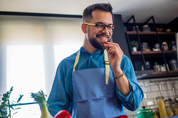 istock A young, smiling man in the kitchen is cutting vegetables on a board, radiating joy and relaxation. 2207167843
