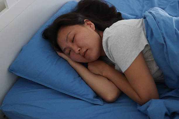 istock Young asian woman sleeping peacefully in bed on blue sheets 2207169448