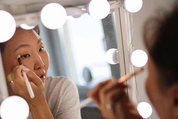 istock Asian woman applying makeup in front of mirror with lights 2207176477