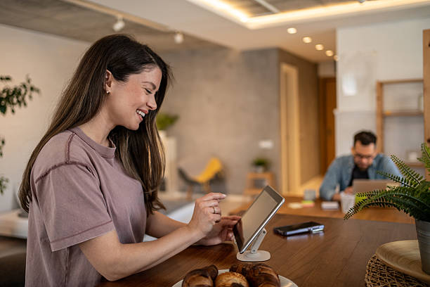 istock Smiling woman using digital tablet at home with partner working in background 2207177375