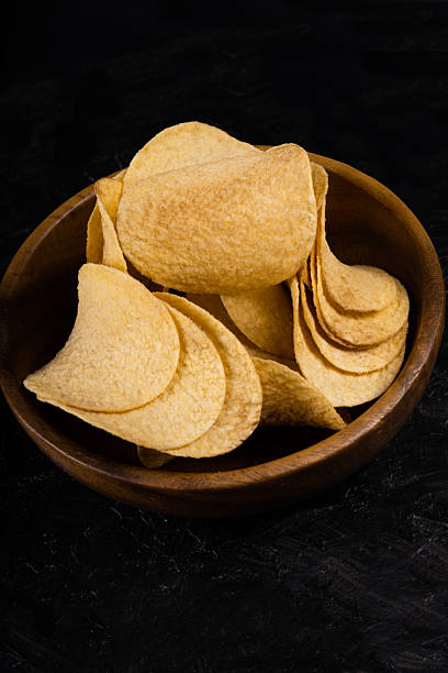 Bowl of crispy potato chips on a dark background. Simple and tasty snack for any occasion.