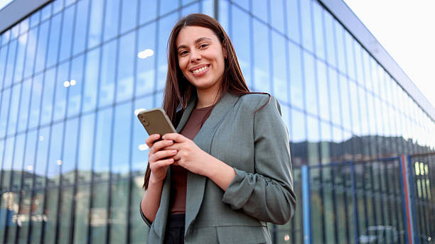 istock Smiling businesswoman using smartphone in front of modern office building 2207180252
