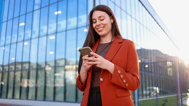 istock Smiling businesswoman using smartphone in front of modern office building 2207180253