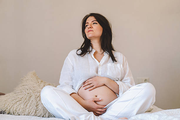 Pregnant woman sitting peacefully on bed in cozy home setting