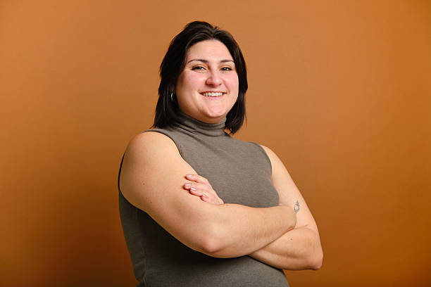 istock Young plus-size woman smiling with folded arms looking at the camera on brown background 2207189012