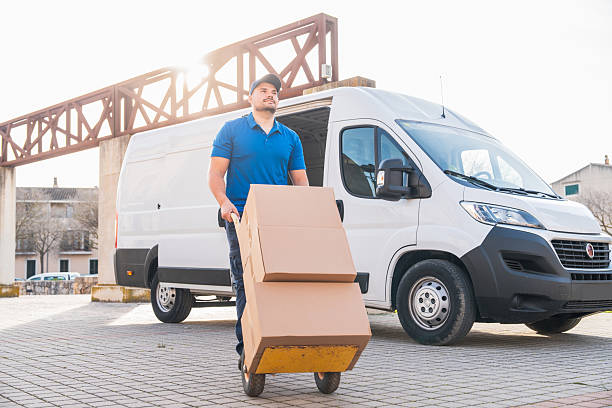 istock Courier Moving Boxes with Hand Truck in Front of Van 2207198935
