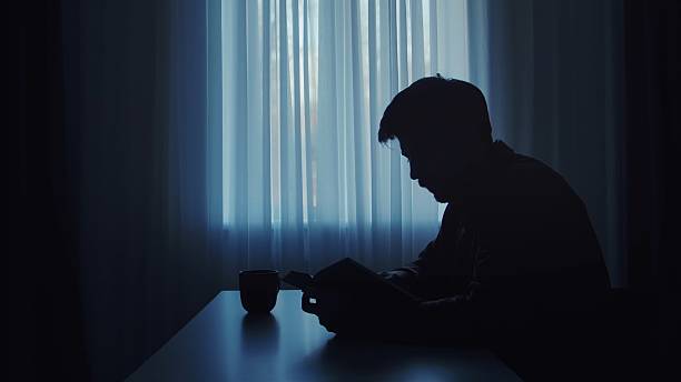 istock Silhouette of a Man Reading Near a Window 2207201467