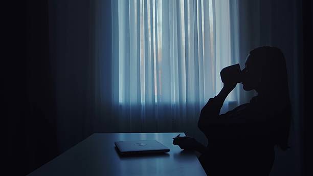istock Silhouette of person drinking coffee by window with laptop 2207201656