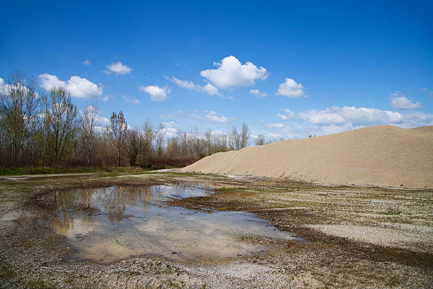 Excavated sand and gravel piles from quarry operations, processed by heavy machinery at an industrial site.