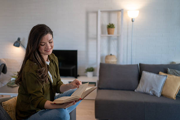 istock Young woman reading a book at home on the sofa 2207206165