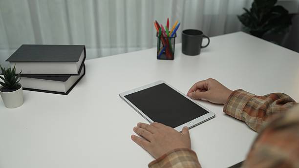A person is using a tablet in a modern workspace, surrounded by notebooks, office supplies, and a green plant, creating an inspiring environment for productivity.