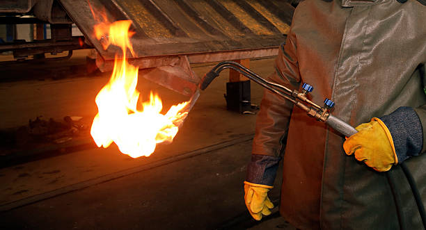 Worker uses a flame torch to melt metal in a manufacturing facility during evening hours