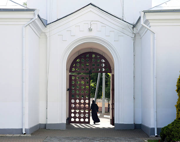 A monk dressed in traditional attire walks through an intricately designed wooden gate, surrounded by serene architecture and greenery.