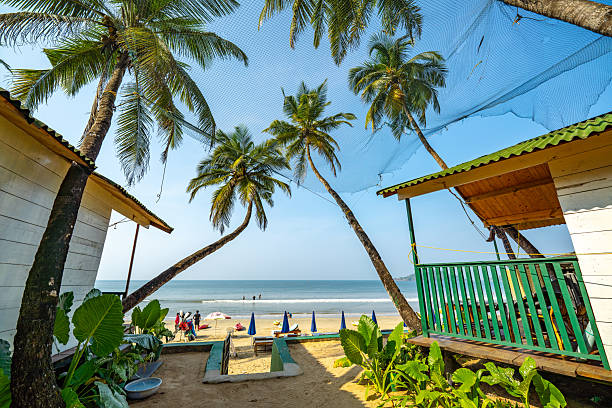 Typical peaceful, tranquil Goan beach scene with wind swept coconut, palm trees, golden sand, old shack, a structure with a cross and clear blue tropical sky.