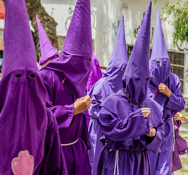 Quito, Pichincha, Ecuador - April 15, 2022: Penitents in purple robes and chains, walking during the Jesus del Gran Poder procession in Holy Week in Quito, Ecuador