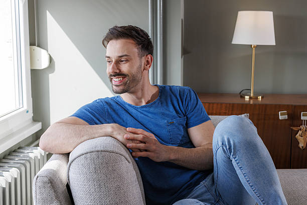 istock Man relaxing on sofa with a cheerful smile, enjoying a calm daytime indoors 2207229304
