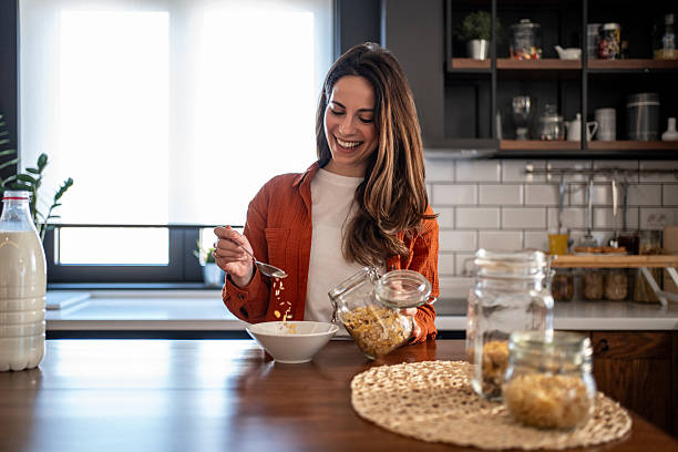 istock Young woman pouring cereals into bowl for breakfast in modern kitchen 2207233333