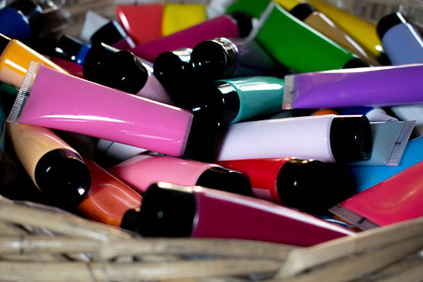 Tubes of acrylic paint in various shades of red and pink are arranged side by side. Two paintbrushes with red handles and golden ferrules cross over the tubes. The brush bristles appear clean and dry, suggesting they are ready for use. The smooth, shiny surface of the paint tubes contrasts with the soft texture of the brushes, creating a visually appealing composition ideal for artistic inspiration.
